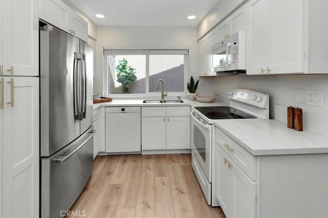 kitchen with a sink, light wood finished floors, white appliances, white cabinetry, and recessed lighting