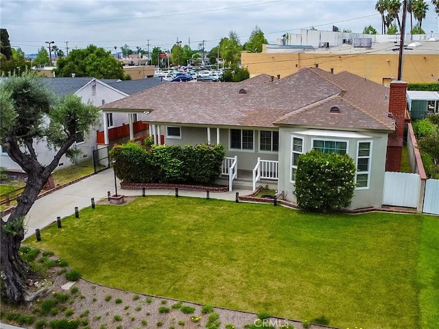 rear view of property with a lawn, roof with shingles, stucco siding, and fence