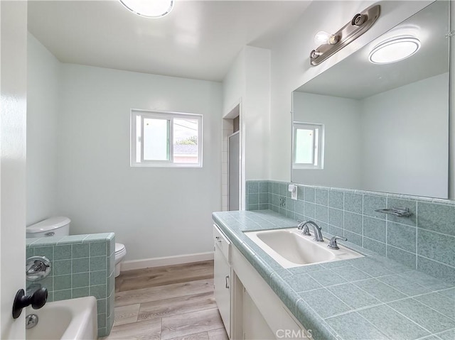 full bathroom with wood finished floors, toilet, a healthy amount of sunlight, and vanity