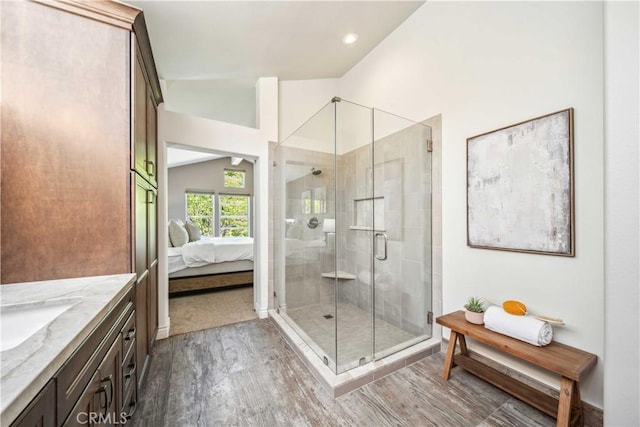 ensuite bathroom featuring wood finished floors, a shower stall, lofted ceiling, and vanity