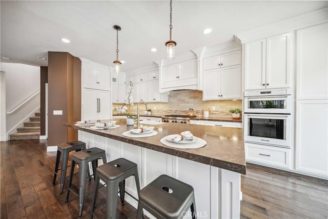 kitchen featuring recessed lighting, white cabinets, dark wood finished floors, backsplash, and a breakfast bar