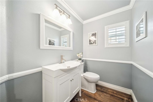 half bath featuring crown molding, wood finished floors, toilet, vanity, and baseboards
