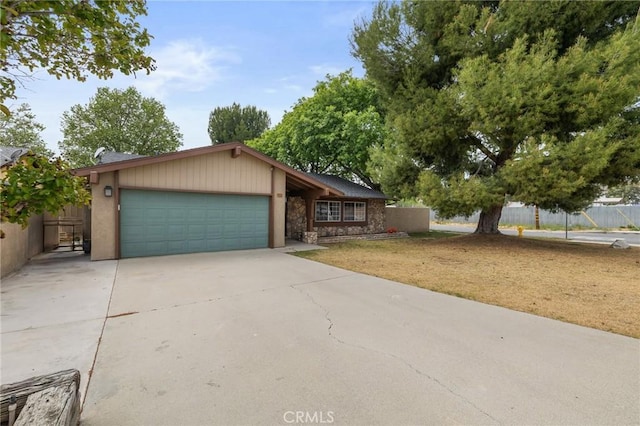 view of front facade featuring an attached garage, fence, stone siding, and concrete driveway
