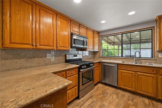 kitchen with brown cabinetry, appliances with stainless steel finishes, tasteful backsplash, a sink, and light wood-style floors