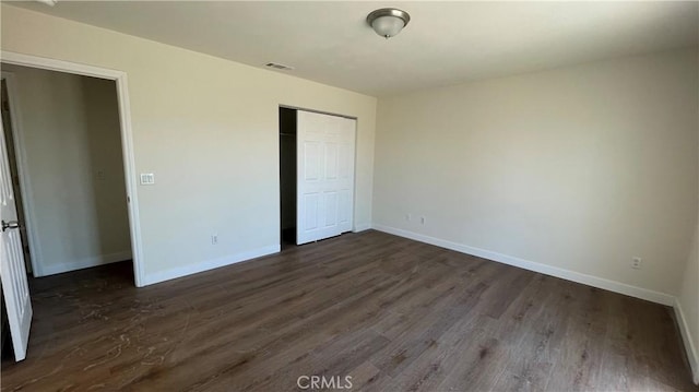 unfurnished bedroom featuring a closet, baseboards, dark wood-type flooring, and visible vents