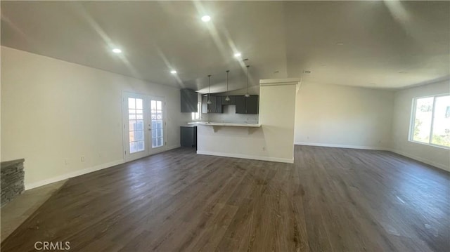 unfurnished living room with baseboards, vaulted ceiling, dark wood-style flooring, and a wealth of natural light