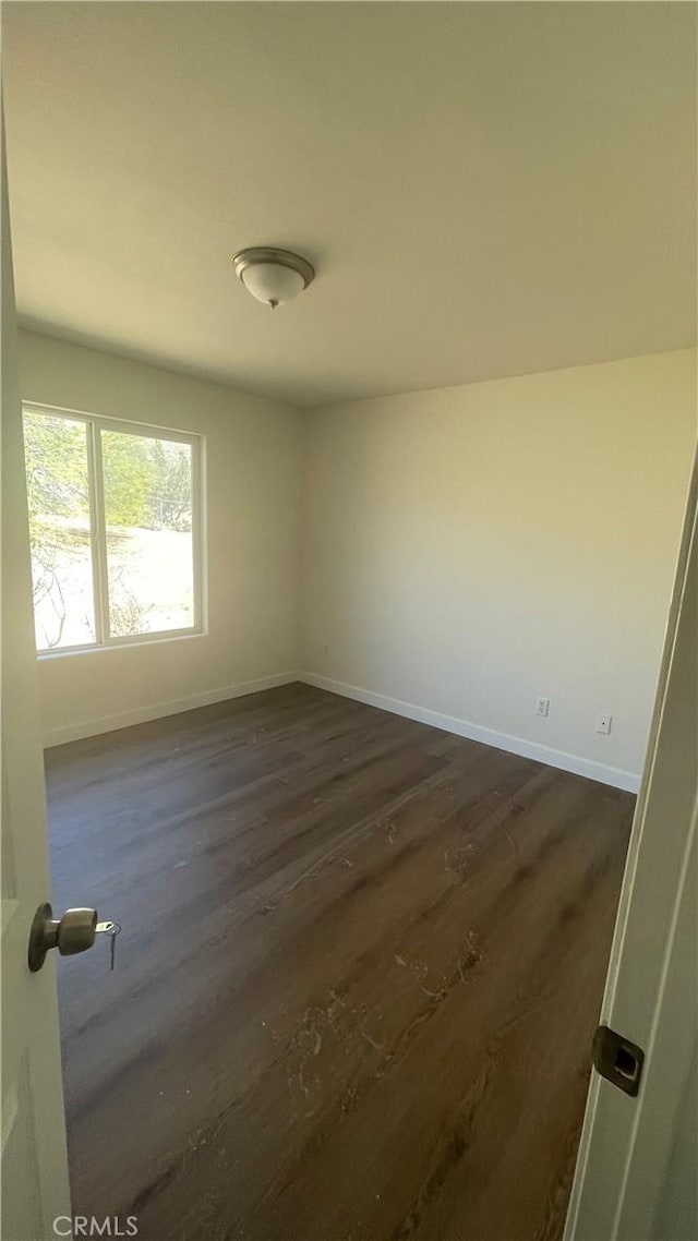 unfurnished room with baseboards and dark wood-style flooring