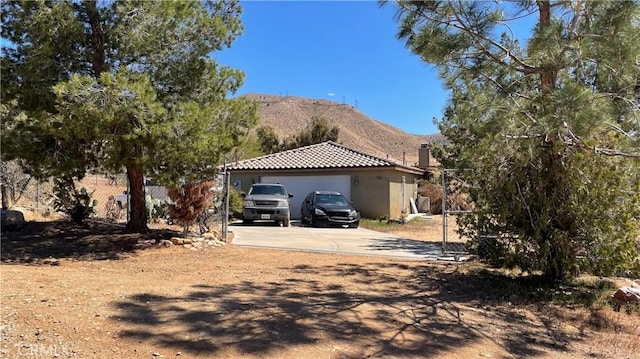 view of front facade with fence, an attached garage, stucco siding, a mountain view, and driveway
