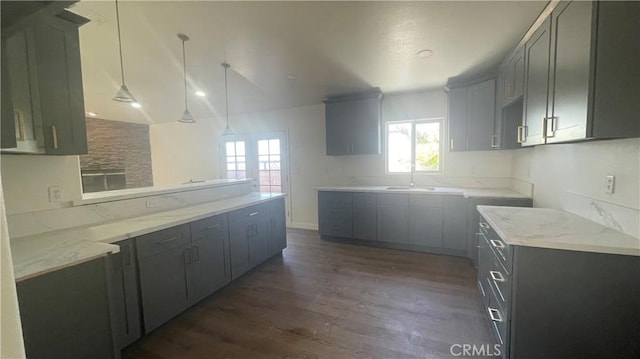 kitchen with light stone countertops, a wealth of natural light, a sink, and dark wood-type flooring