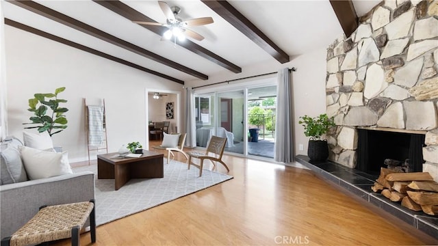 living room with a ceiling fan, lofted ceiling with beams, a stone fireplace, and wood finished floors
