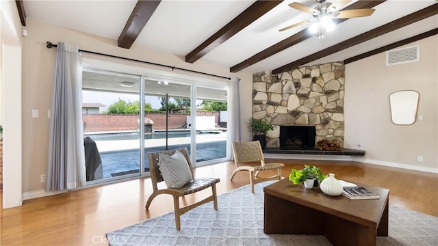 living room featuring ceiling fan, a stone fireplace, visible vents, wood finished floors, and lofted ceiling with beams