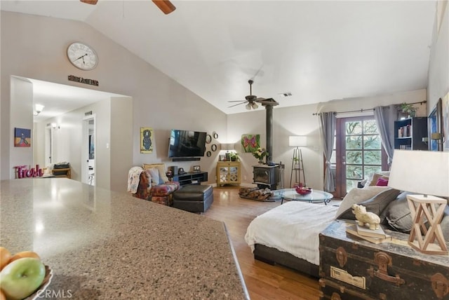bedroom featuring a ceiling fan, high vaulted ceiling, wood finished floors, and a wood stove