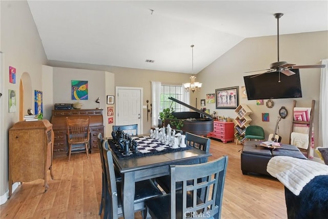 dining space with arched walkways, light wood-style flooring, ceiling fan with notable chandelier, vaulted ceiling, and visible vents