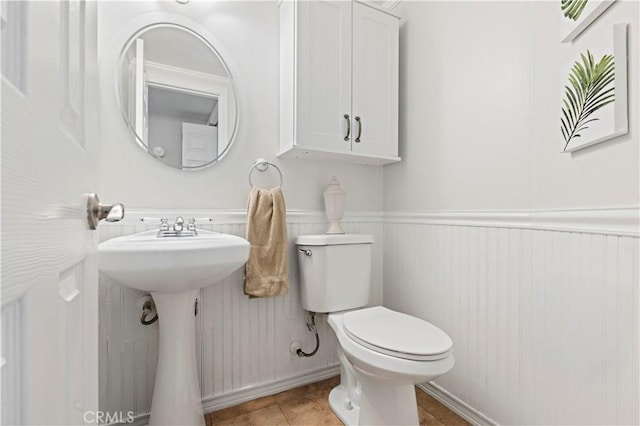 half bathroom featuring tile patterned flooring, wainscoting, and toilet
