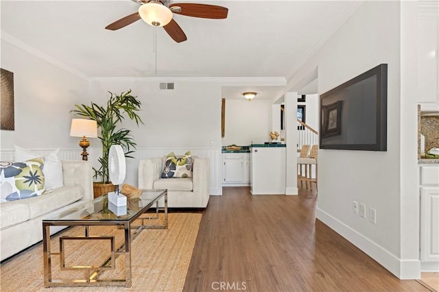 living room with ceiling fan, visible vents, ornamental molding, and wood finished floors