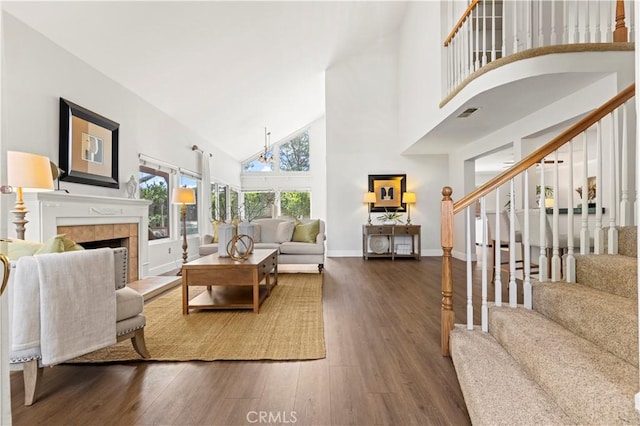 living room with a tiled fireplace, wood finished floors, high vaulted ceiling, baseboards, and stairs