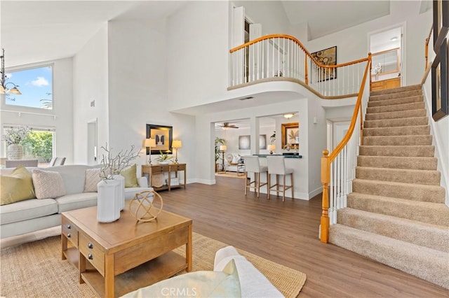 living area featuring stairs, baseboards, wood finished floors, and a towering ceiling