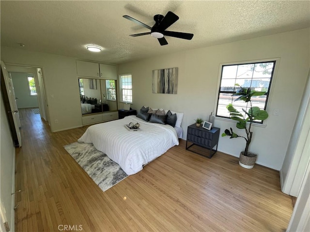 bedroom featuring a ceiling fan, a textured ceiling, baseboards, and light wood finished floors