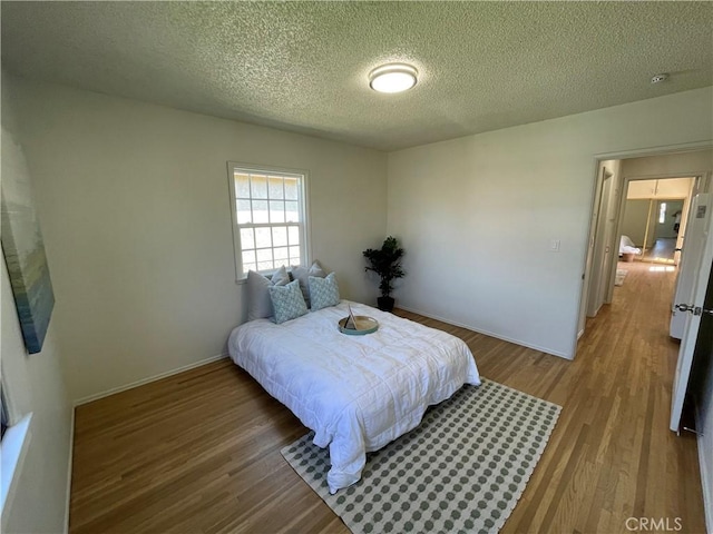 bedroom featuring baseboards, a textured ceiling, and wood finished floors
