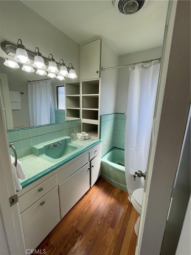 bathroom with vanity, visible vents, wood finished floors, shower / bath combination with curtain, and toilet