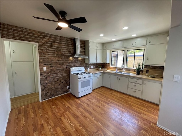kitchen with wall chimney range hood, white range with gas cooktop, a sink, and light countertops