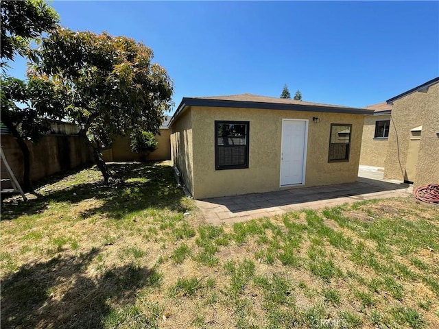 rear view of property with fence, stucco siding, a yard, and a patio area