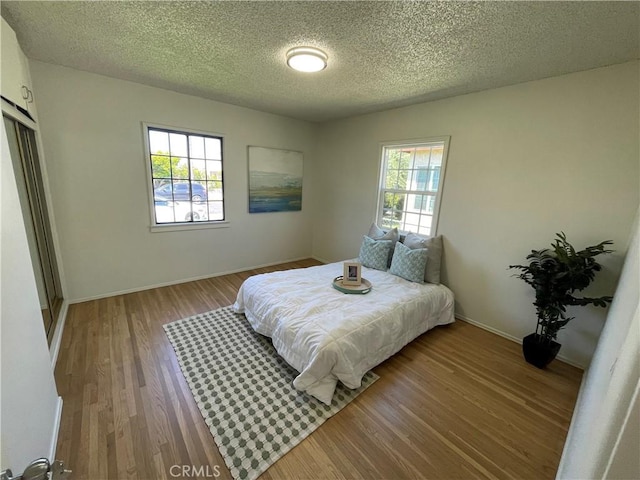 bedroom featuring baseboards, multiple windows, a textured ceiling, and wood finished floors