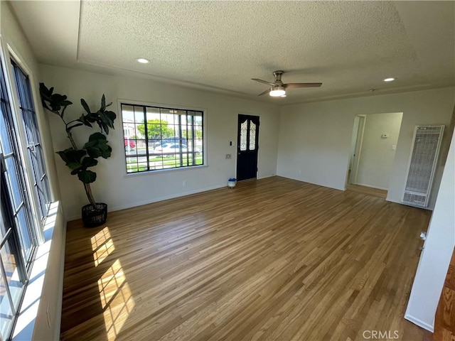 unfurnished living room featuring light wood-style floors, ceiling fan, a textured ceiling, and a heating unit