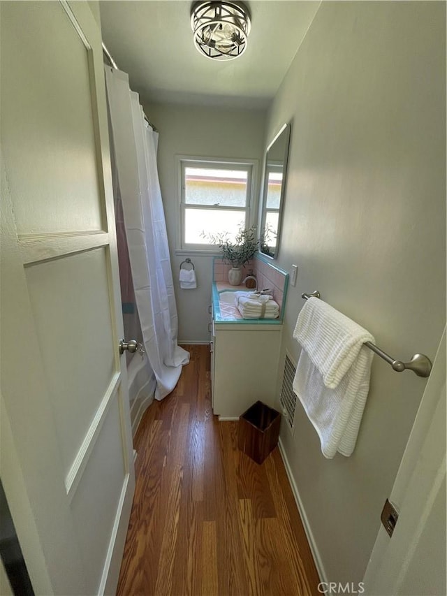 full bath with a sink, baseboards, wood finished floors, shower / tub combo, and visible vents