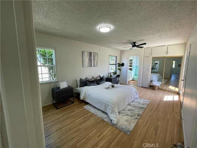 bedroom with light wood-style floors, a textured ceiling, baseboards, and multiple windows