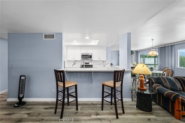 1530 Greenbriar Ave, Corona, CA 92878 - kitchen with stainless steel appliances, wood finished floors, a kitchen breakfast bar, visible vents, and white cabinets