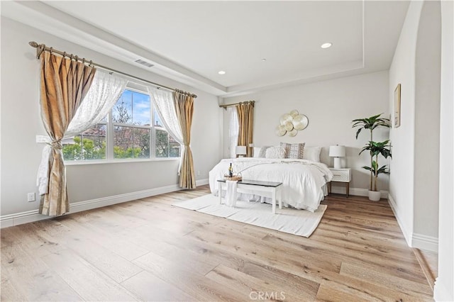 bedroom with baseboards, a tray ceiling, wood finished floors, and visible vents