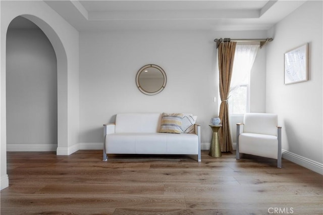 sitting room featuring baseboards, arched walkways, wood finished floors, and a tray ceiling