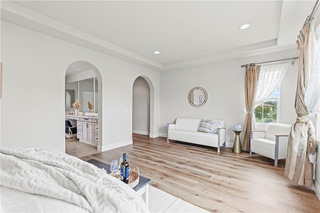 bedroom with recessed lighting, arched walkways, a raised ceiling, and light wood-style flooring