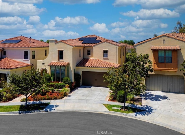 mediterranean / spanish-style house with an attached garage, roof mounted solar panels, and concrete driveway