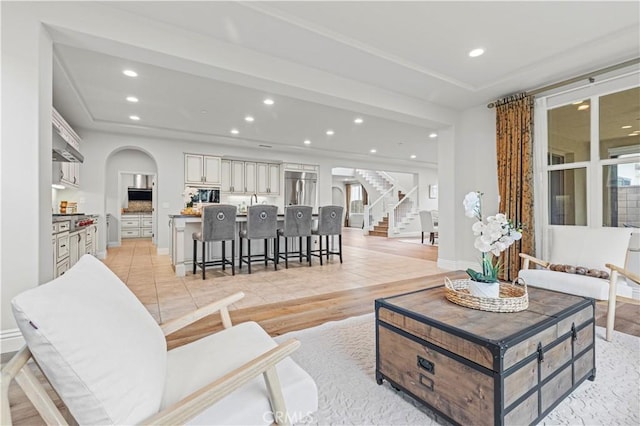 living room featuring arched walkways, light wood-style flooring, recessed lighting, baseboards, and stairway