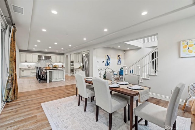 dining area with light wood-style floors, arched walkways, recessed lighting, and visible vents