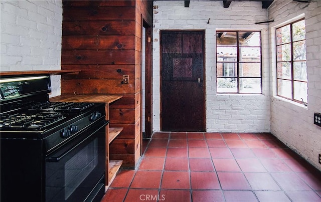 kitchen featuring dark tile patterned flooring, black gas stove, and brick wall