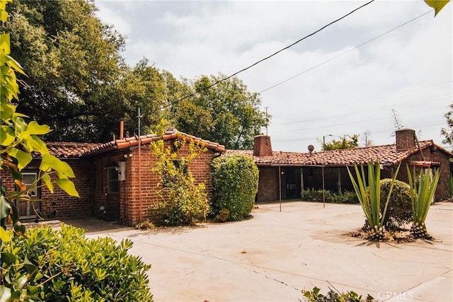 view of front of home featuring a tiled roof, a chimney, and brick siding