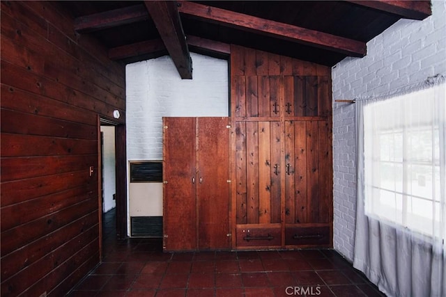 empty room with wooden walls, dark tile patterned floors, lofted ceiling with beams, and a healthy amount of sunlight