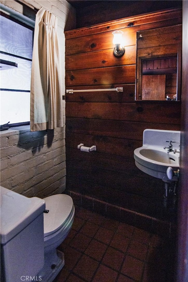 bathroom featuring a sink, toilet, and wooden walls