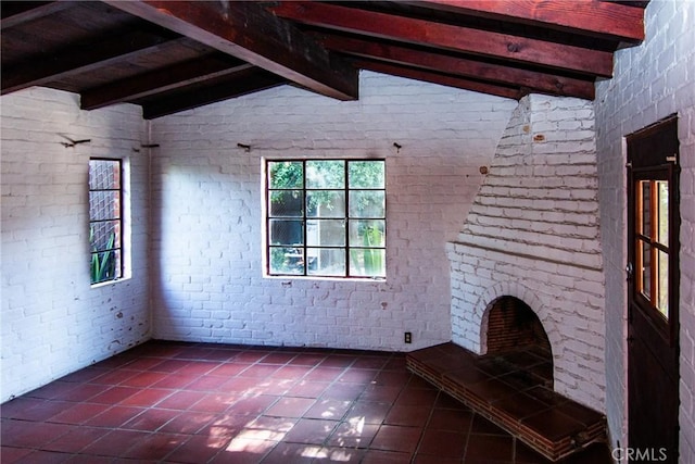 unfurnished living room featuring vaulted ceiling with beams, dark tile patterned floors, and brick wall