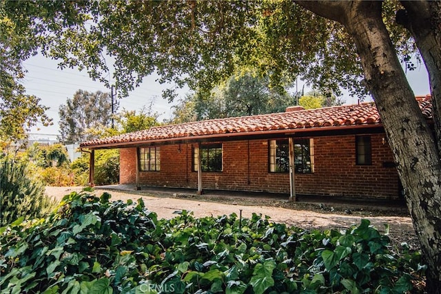 back of house featuring a tiled roof and brick siding