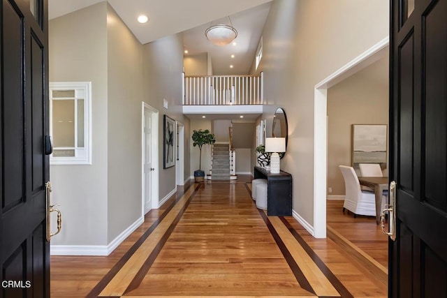 entryway featuring baseboards, recessed lighting, light wood-style flooring, and a high ceiling