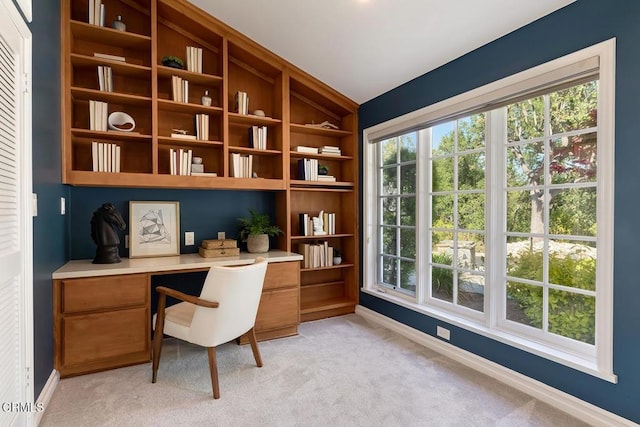 home office featuring built in study area, baseboards, and light colored carpet