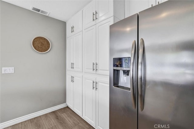 kitchen featuring white cabinets, stainless steel fridge, baseboards, wood finished floors, and visible vents