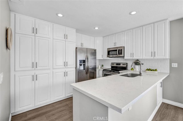 kitchen featuring a peninsula, wood finished floors, white cabinets, a sink, and stainless steel appliances