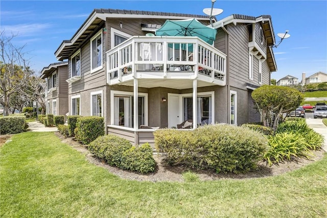 rear view of property with a lawn, stucco siding, and a balcony
