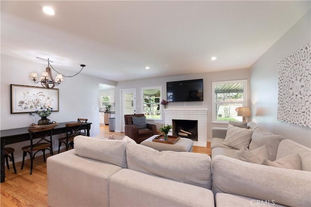 living room with recessed lighting, a notable chandelier, a fireplace, and light wood-type flooring
