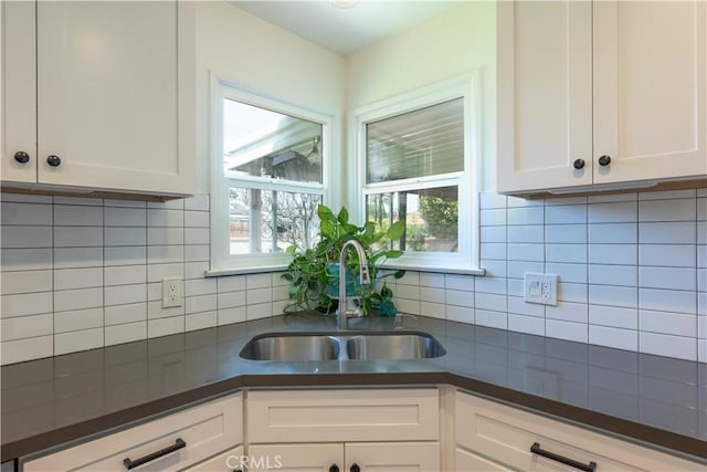 kitchen featuring a sink, white cabinetry, decorative backsplash, and dark countertops
